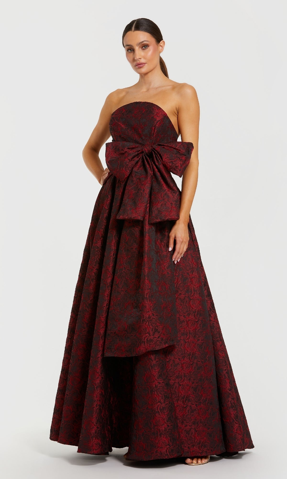 Woman wearing a burgundy strapless gown with a large bow on a white background